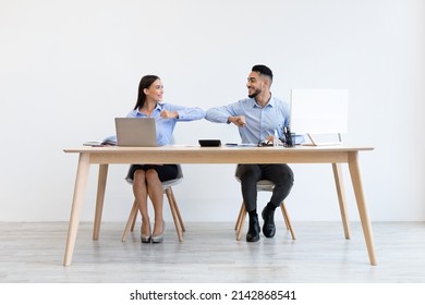 Social-Distancing Business Greeting. Smiling diverse colleagues greeting each other tapping bumpimg elbows sitting at desk. People avoid handshake and touch. Back to office after self-isolation - Powered by Shutterstock