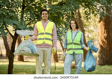 A socially active diverse loving couple in safety vests and gloves, holding bags of garbage while cleaning up the park together. - Powered by Shutterstock