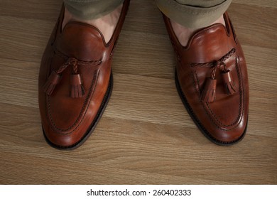 Sockless Male Legs In Tasseled Loafers, Dark Leaf Colored And Burnished. Preppy Style Dressed Man Wearing Cushioned Pants And Loafers