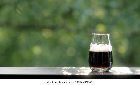 Soda or fizzy cold drink in a glass on a green background with trees. Evening making drinks with bubbles outdoors. Lemonade is poured in a glass goblet. Foam settles in a glass of drink