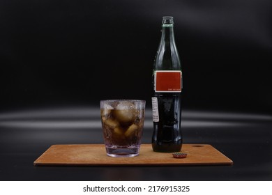 Soda And Ice In A Clear Plastic Cup Next To A Glass Soda Bottle With A Blank Red Label.