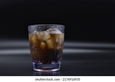 Soda And Ice In A Clear Plastic Cup On A Black Background.