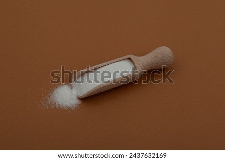Sodium erythorbate or sodium isoascorbate in wooden scoop on brown background. White powder with chemical formula C6H7NaO6. Food additive E316  used in meats, poultry and soft drinks.