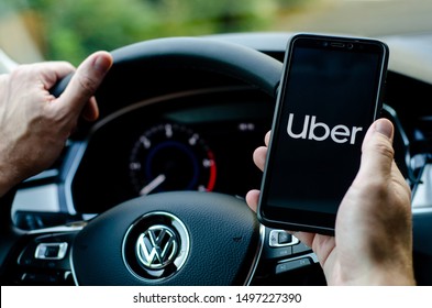 Soest, Germany - August 4, 2019: Uber driver holding smartphone in Volkswagen car. Uber is an American company offering transportation services online.