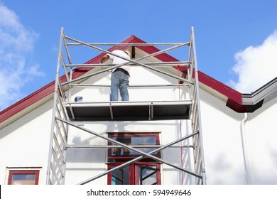 SOEST, NETHERLANDS - August 12, 2016. Man On Scaffold Tower Is Painting And Renovating Exterior Walls And Window Frames Of Old Dutch House, Working Outdoors With Tools And Equipment Under Blue Sky.  