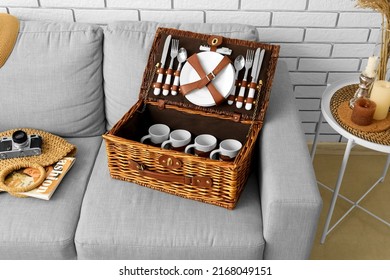 Sofa With Basket For Picnic, Photo Camera And Bag Near White Brick Wall