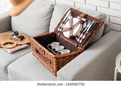 Sofa With Basket For Picnic, Photo Camera And Bag Near White Brick Wall