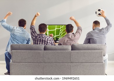 Sofa experts. Back view of male friends gathered at home to watch a football match sitting on the couch in front of the big screen TV. Men actively support their favorite team and comment on the match