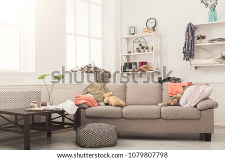 Sofa in messy living room with many stack of clothes. Disorder and mess at home, copy space