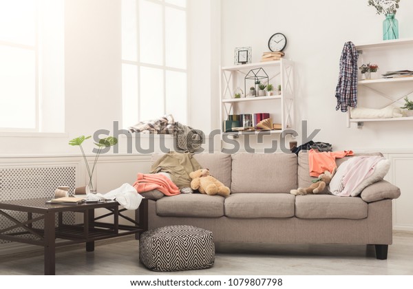 Sofa in messy living room with many\
stack of clothes. Disorder and mess at home, copy\
space