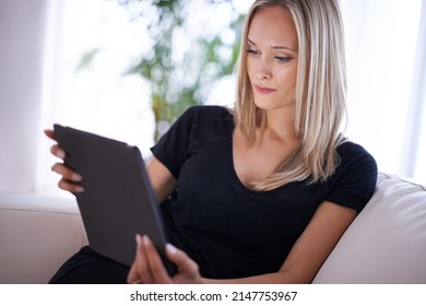 Sofa surfing. Shot of a young blonde woman relaxing at home with her digital tablet.