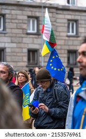Sofia, Bulgaria - April 28, 2022: A man with three flags is looking in his smartphone 