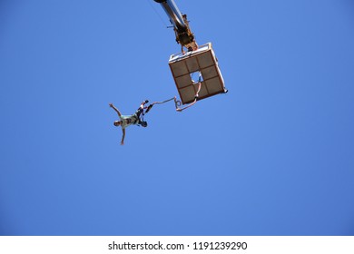 Sofia, Bulgaria - September 22, 2018: Bungee Jumping From A 50-metre-high Crane During Sofia Extreme Sports Festival. Seen From The Ground Young Woman Rushing Down From A Platform High In The Blue Sky