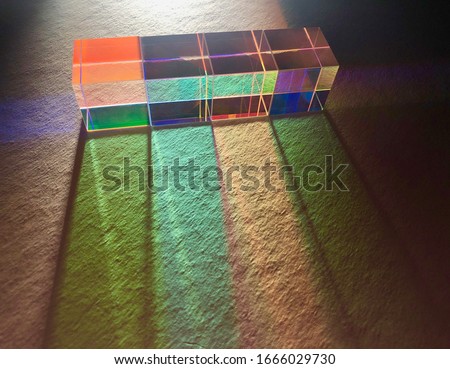 Soft artificial light shines from backside through a row of square dichroic cubes with mirror surface dispersing light into colourful spectrums on texture white paper. 