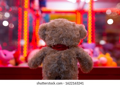 A soft bear stands with its back and looks sad at a slot machine with soft toys. Red tone
