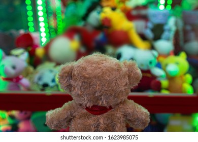 A soft bear stands with its back and looks sad at a slot machine with soft toys. Green tone.
