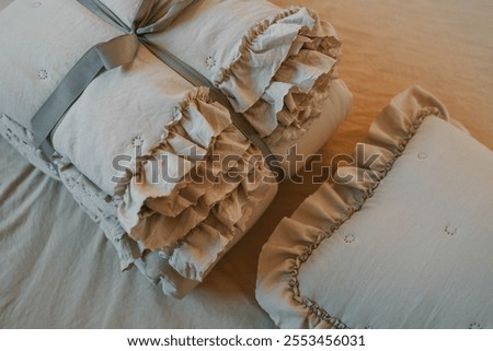 Soft beige bedding set with ruffled details tied with a gray ribbon on a matching beige background. Perfect for themes of comfort, elegance, and minimalistic home decor.