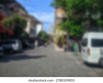 A soft blurred background view of a quiet street with parked cars and buildings on a bright sunny summer day.