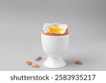 Soft boiled egg in cup and eggshell on light grey background