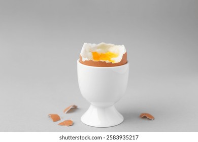Soft boiled egg in cup and eggshell on light grey background
