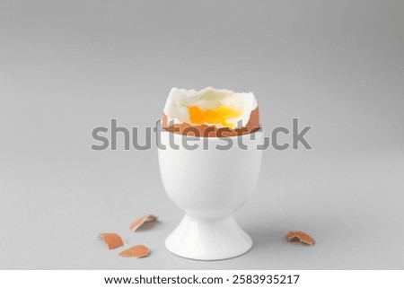 Soft boiled egg in cup and eggshell on light grey background
