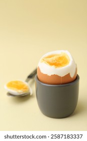Soft boiled egg in eggcup and spoon on beige background, closeup