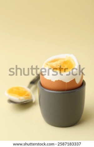 Soft boiled egg in eggcup and spoon on beige background, closeup