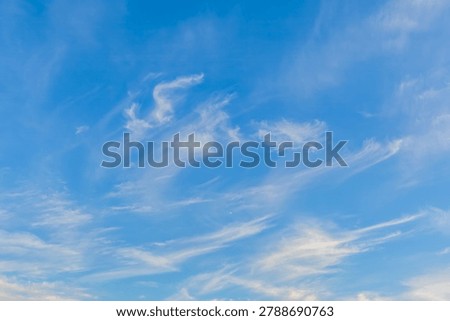 Soft cloud formations drift across a clear blue afternoon sky, creating a calm and peaceful atmospheric scene.