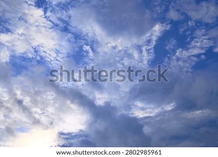 Soft clouds drift across a vast, clear blue sky. Sunlight glows gently behind scattered white formations. Calm atmosphere invites peace and quiet contemplation