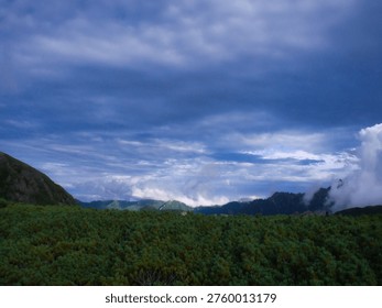 Soft clouds drift over the mountains as layers of ridges fade gently into the distant sky.