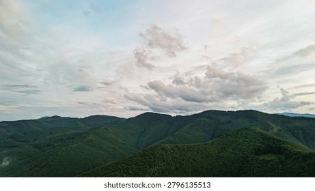 Soft clouds sweep above rolling green ridges as evening light fades across expansive mountains captured from a drone showing layered horizons quiet forests and the calm mood of remote highlands