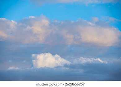 Soft clusters of cotton like clouds drift across a vivid sky, revealing patches of pale blue between them. Hints of gentle warm sunlight touch their edges with a faint glow.