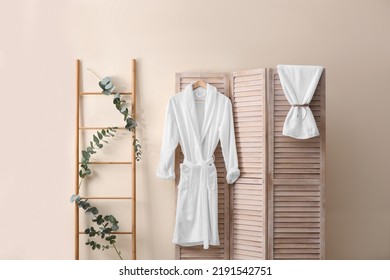 Soft comfortable bathrobe hanging on folding screen in stylish room interior