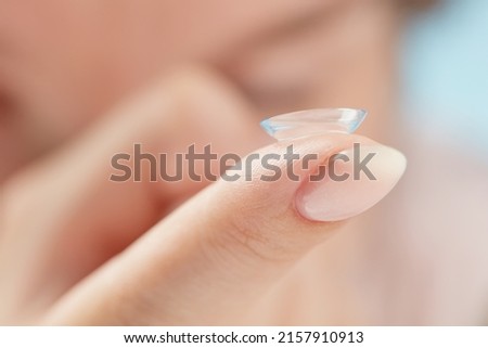 Soft contact lens on female finger against the blurred face, close up. Medicine and vision concept. Woman putting soft contact lens into eye. Shallow depth of field.