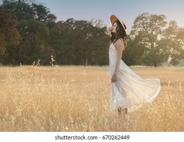 Soft And Dreamy Image Of A Young Woman With Blowing Dress In Grassy Field At Sunset