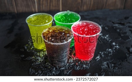 A lot of Soft drinks in colorful and flavorful plastic glasses with ice cubes Chilled on ice on the black background, Soft drinks or Carbonated beverages on ice