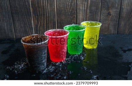 A lot of Soft drinks in colorful and flavorful plastic glasses with ice cubes Chilled on ice on the black background, Soft drinks or Carbonated beverages on ice