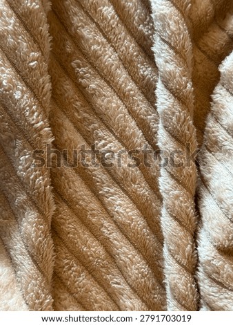 Soft fabric surface in creamy‑brown tones with deep, parallel diagonal ridges, plush and fluffy texture; bright creamy‑white accents, warm, cozy, softly shiny, with neat and luxurious pattern.