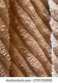 Soft fabric surface in golden‑brown tones with parallel diagonal ridges, plush dense texture, and a bright creamy‑white stripe; warm, fluffy, softly shiny, with neat, comfortable pattern.