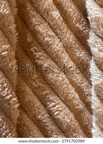 Soft fabric surface in golden‑brown tones with parallel diagonal ridges, plush dense texture, and a bright creamy‑white stripe; warm, fluffy, softly shiny, with neat, comfortable pattern.