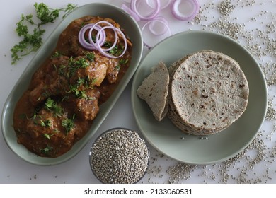Soft flat bread made of pearl millet flour. Served with chicken in cashew gravy garnished with fresh coriander leaves. Shot on white background. Commonly called bajra roti and chicken curry in India