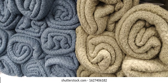 Soft fluffy beige, gray and blue plaids, rolled up in skeins, rolls and bundles. An assortment of different bedspreads on a store shelf. The blankets are beautifully laid out for sale. Fleecy fabric