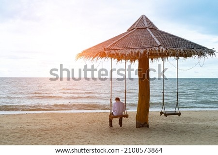 soft focus of alone man to sit on swings with rope is under  wooden stand bower on the beach and sunlight background