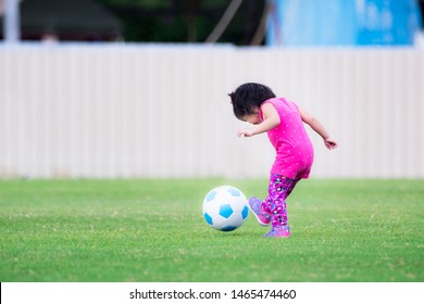 Soft Focus. Asian Baby Child Girl Ages 2 Years 5 Months. She Is Kicking A Blue-white Soccer Football On A Green Lawn. Sweet Smile. Happy Kid Running And Exercise In The Everning.