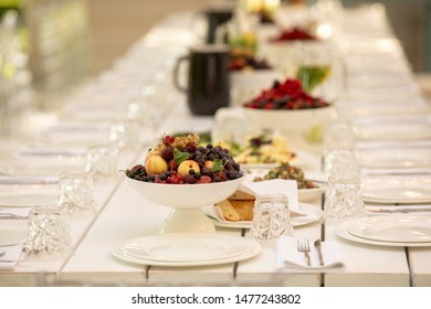 Soft Focus Of Big Fruit Bowl On Long Banquet Table Served With Plates, Cutlery And Glasses In Restaurant