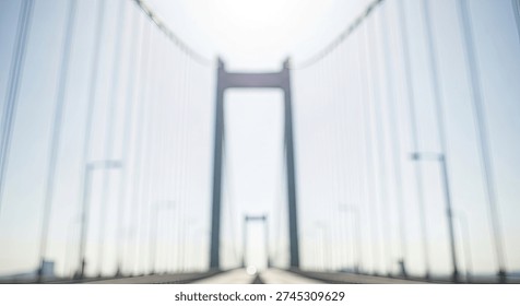 A soft focus, blurred image of a large suspension bridge, emphasizing its towering structure and cables, with a bright, almost ethereal sky in the background, suggesting movement and a sense of journ.