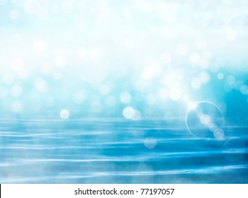 Soft focus bokeh light effects over a rippled, blue water background with  lens flare.