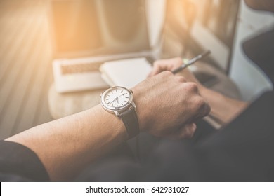 soft focus businessman looking at his watch on his hand, watching the time and writing something on note book.computer laptop on wooden desk - Powered by Shutterstock