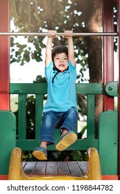 Soft Focus And Close Up The Asian Kid Wearing Helmet And Using Two Hand Holding Monkey Bar To Lift Up In The Air. The Asia Boy Play In The Playground. Concept Happy Kids, Activity And Safety Exercise.