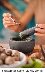 Soft focus of crop female adding spoonful of olive oil to mortar with mojo de cilantro sauce while cooking papas de tenerife dish for lunch